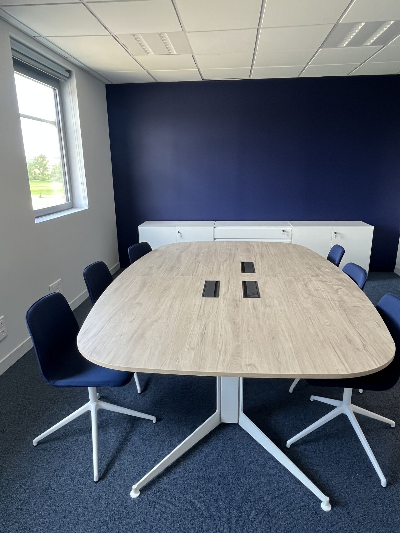 Salle de réunion aux tons bleu marine avec table ovale en bois clair aménagée par I Log You